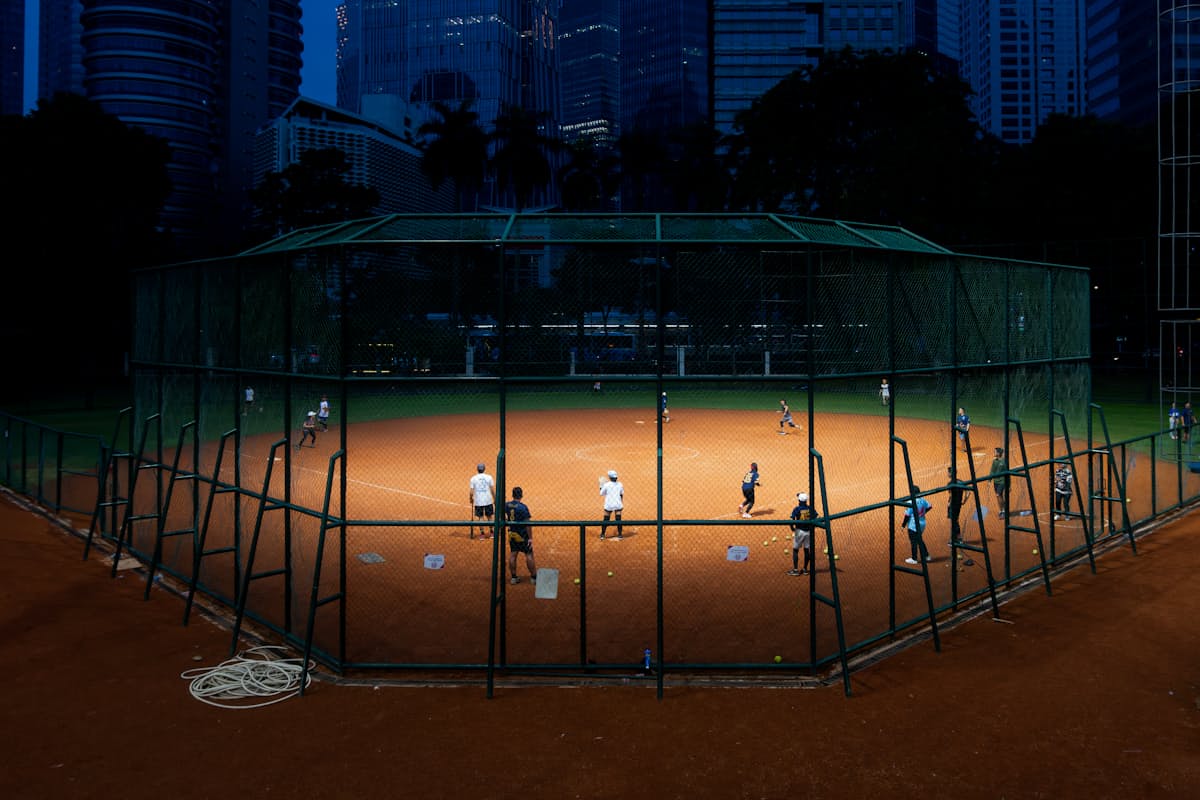 Softball diamond lit up at night beneath a city skyline